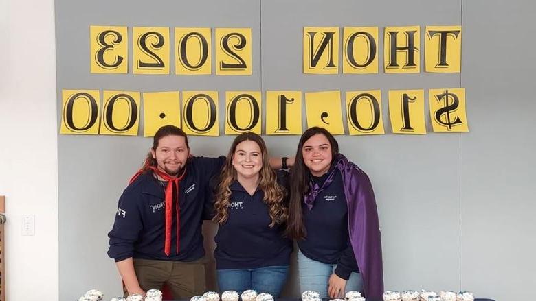 Three students stand smiling by table