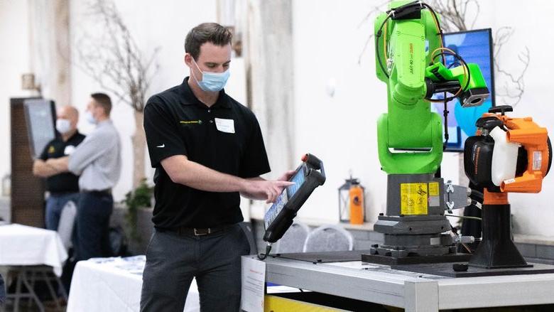 Man wearing mask holds digital tablet in front of robotic arm